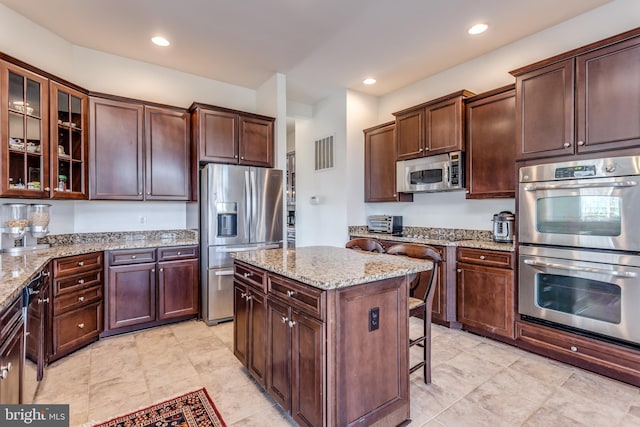 kitchen with light stone counters, a breakfast bar, dark brown cabinets, stainless steel appliances, and a center island