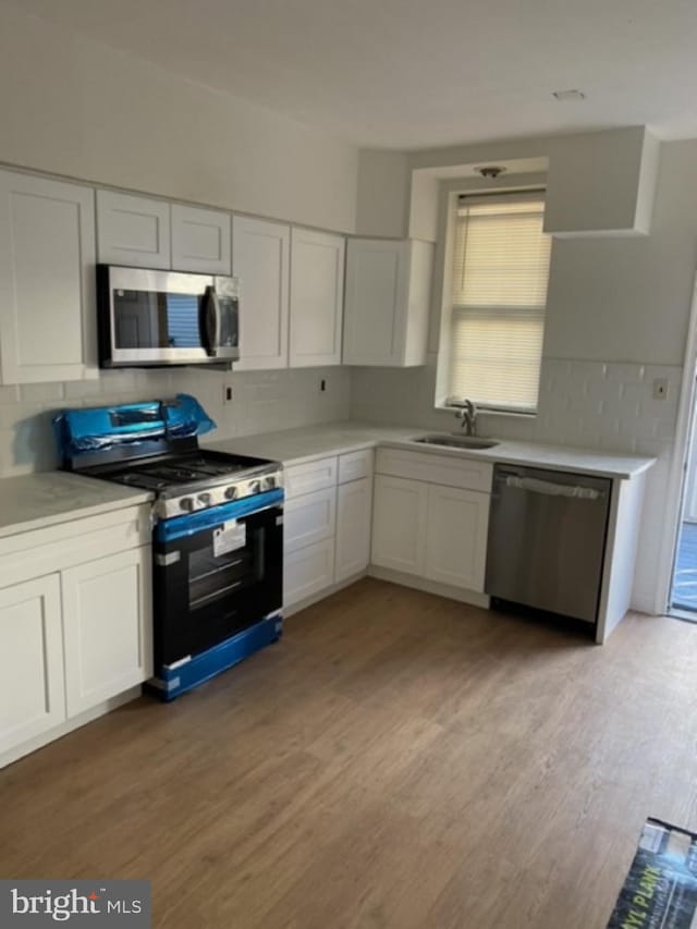 kitchen with light wood-type flooring, stainless steel appliances, white cabinetry, and sink