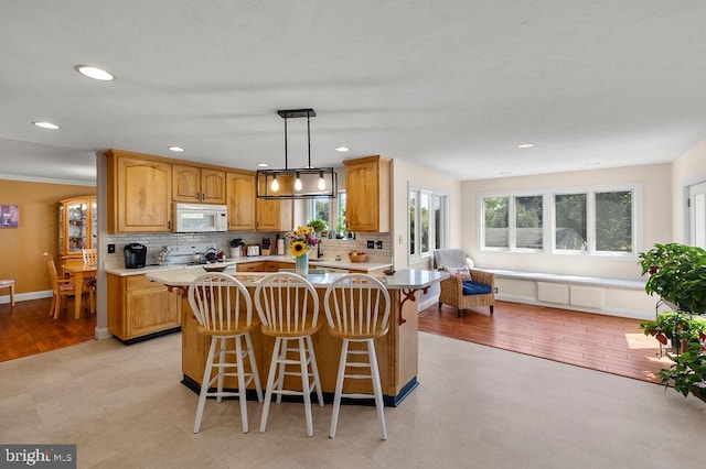 kitchen with hanging light fixtures, light hardwood / wood-style floors, a breakfast bar area, a kitchen island, and decorative backsplash