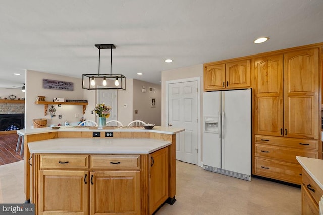 kitchen featuring pendant lighting, a stone fireplace, a center island, white fridge with ice dispenser, and ceiling fan