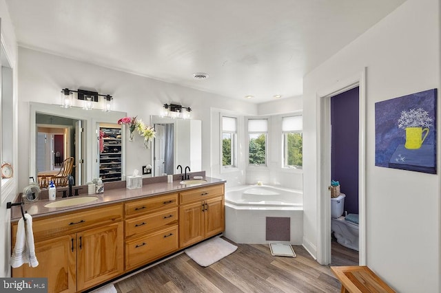 bathroom featuring toilet, hardwood / wood-style flooring, tiled bath, and vanity