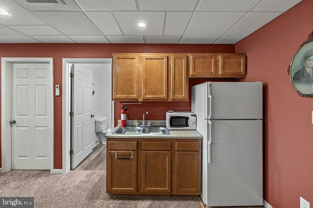 kitchen with a paneled ceiling, white appliances, light carpet, and sink