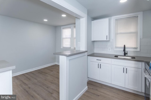 kitchen with tasteful backsplash, sink, white cabinetry, kitchen peninsula, and light hardwood / wood-style flooring