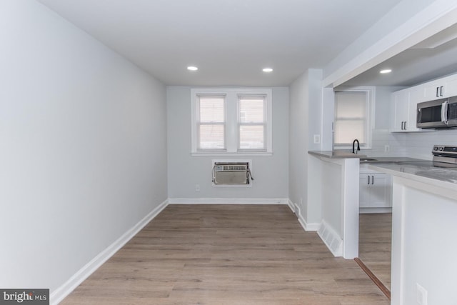 kitchen featuring white cabinets, sink, stainless steel appliances, light hardwood / wood-style floors, and an AC wall unit