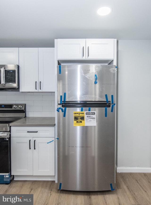 kitchen with appliances with stainless steel finishes, light hardwood / wood-style floors, white cabinetry, and tasteful backsplash