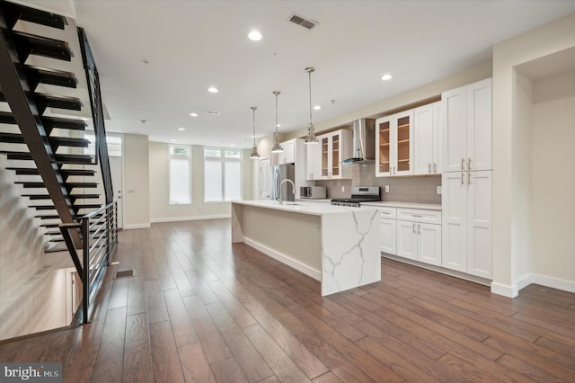 kitchen featuring a center island with sink, appliances with stainless steel finishes, dark wood-type flooring, and wall chimney range hood