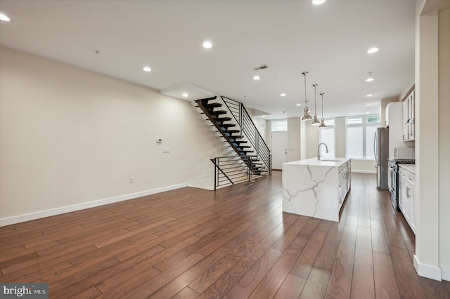 kitchen featuring white cabinets, dark hardwood / wood-style flooring, decorative light fixtures, a kitchen island with sink, and sink