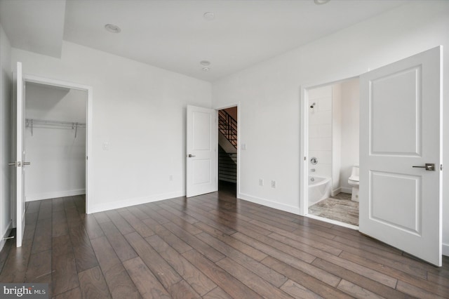 unfurnished bedroom featuring connected bathroom, a closet, a walk in closet, and dark hardwood / wood-style floors