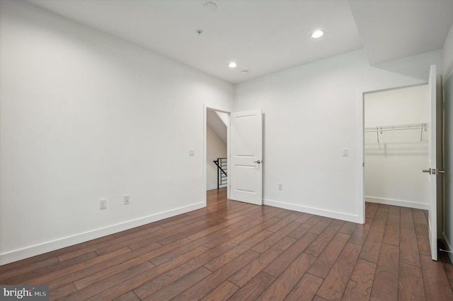 unfurnished bedroom featuring dark wood-type flooring, a walk in closet, and a closet