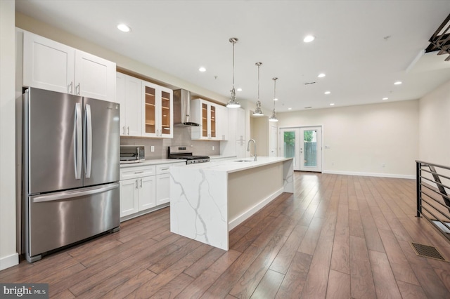 kitchen with dark wood-type flooring, light stone countertops, stainless steel appliances, a center island with sink, and wall chimney range hood