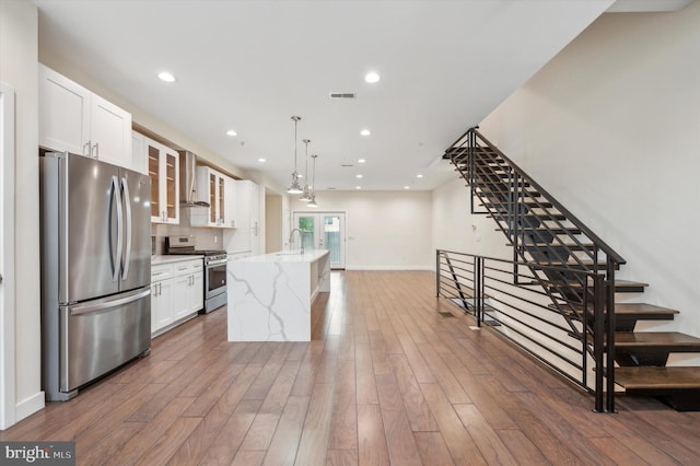 kitchen featuring an island with sink, white cabinetry, appliances with stainless steel finishes, and wall chimney range hood