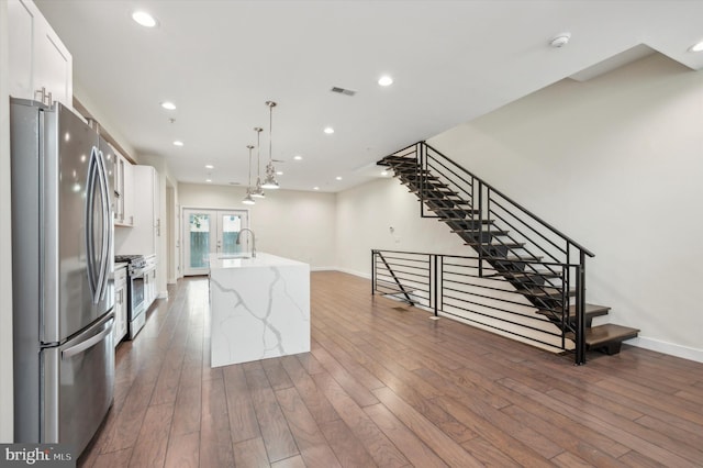 kitchen with appliances with stainless steel finishes, white cabinetry, dark hardwood / wood-style flooring, pendant lighting, and a kitchen island with sink