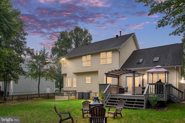 back house at dusk featuring a wooden deck, a gazebo, a pergola, central air condition unit, and a yard