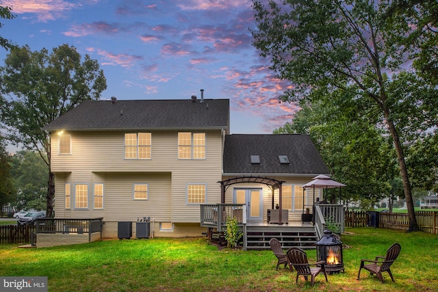 back house at dusk with cooling unit, a deck, and a lawn