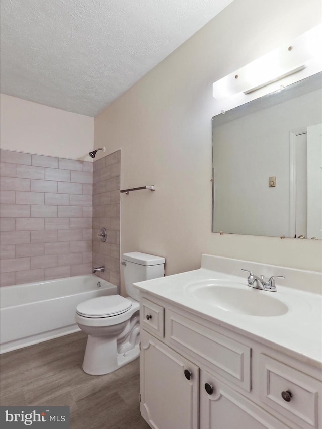 full bathroom featuring vanity, a textured ceiling, tiled shower / bath combo, hardwood / wood-style flooring, and toilet