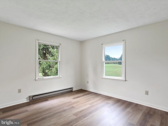 empty room with wood-type flooring, plenty of natural light, and a baseboard radiator