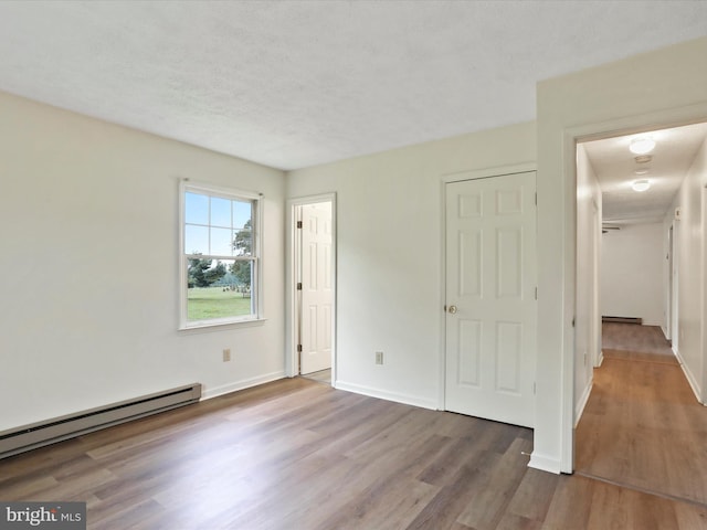 unfurnished bedroom with a textured ceiling, baseboard heating, and hardwood / wood-style floors