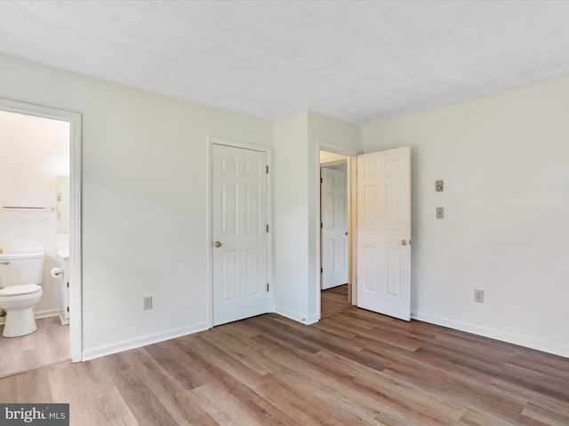 unfurnished bedroom with wood-type flooring and connected bathroom