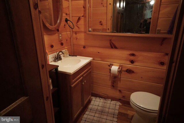 bathroom with wood walls, toilet, and vanity