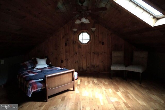 bedroom featuring wood walls, vaulted ceiling with skylight, wood ceiling, and light hardwood / wood-style flooring