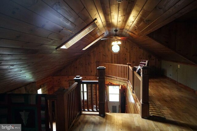 additional living space with vaulted ceiling with skylight, wooden walls, ceiling fan, wood ceiling, and hardwood / wood-style flooring