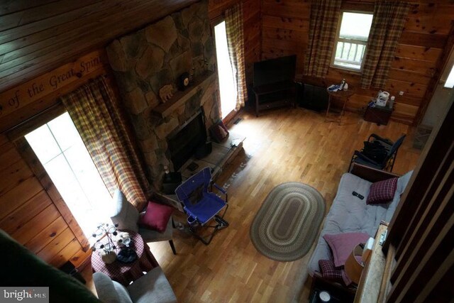 living room with wood walls, a stone fireplace, and light hardwood / wood-style floors