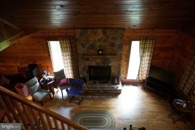 living room with hardwood / wood-style floors, wood walls, and a stone fireplace