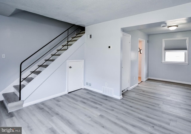 unfurnished living room featuring light wood-type flooring and a textured ceiling