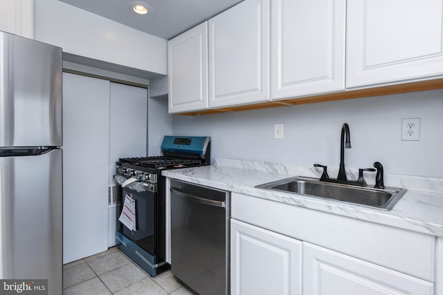 kitchen with appliances with stainless steel finishes, light tile patterned floors, white cabinetry, and sink