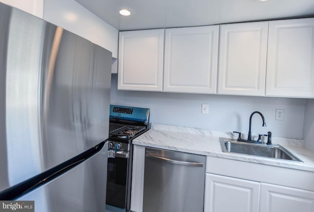 kitchen featuring white cabinets, appliances with stainless steel finishes, light stone countertops, and sink