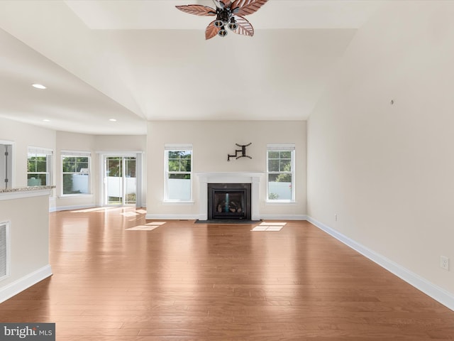 unfurnished living room with a wealth of natural light, ceiling fan, light wood-type flooring, and vaulted ceiling