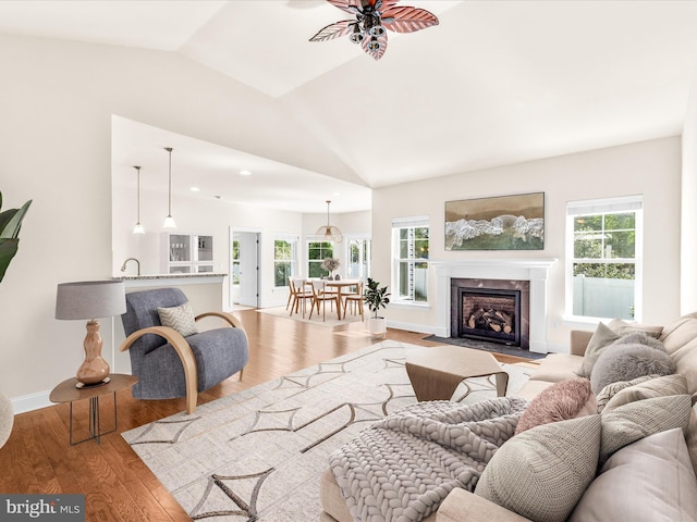 living room with vaulted ceiling, a premium fireplace, sink, ceiling fan, and light wood-type flooring