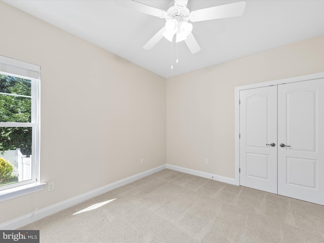 unfurnished bedroom featuring multiple windows, ceiling fan, light colored carpet, and a closet