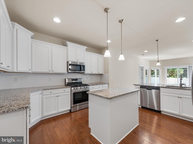 kitchen featuring white cabinets, a center island, stainless steel appliances, dark wood-type flooring, and pendant lighting