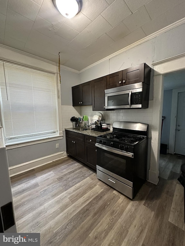 kitchen with dark brown cabinetry, ornamental molding, backsplash, stainless steel appliances, and light wood-type flooring