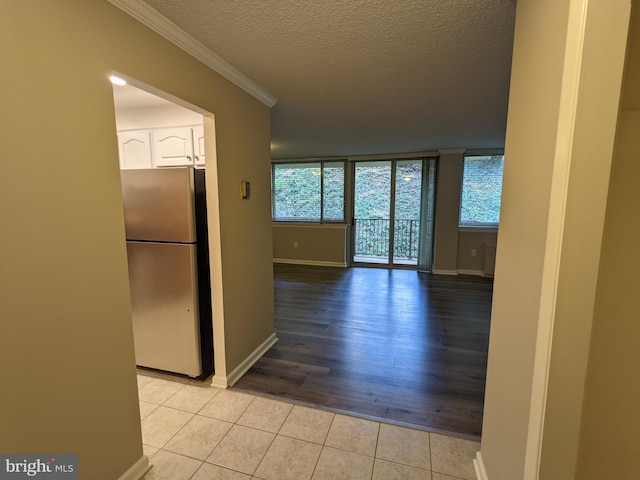 interior space with ornamental molding, a textured ceiling, light hardwood / wood-style flooring, white cabinetry, and stainless steel refrigerator