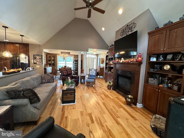 living room with ceiling fan with notable chandelier, a fireplace, ornate columns, light hardwood / wood-style floors, and high vaulted ceiling