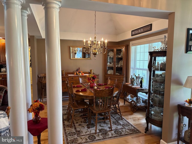 dining area featuring vaulted ceiling, light hardwood / wood-style floors, a notable chandelier, and ornate columns