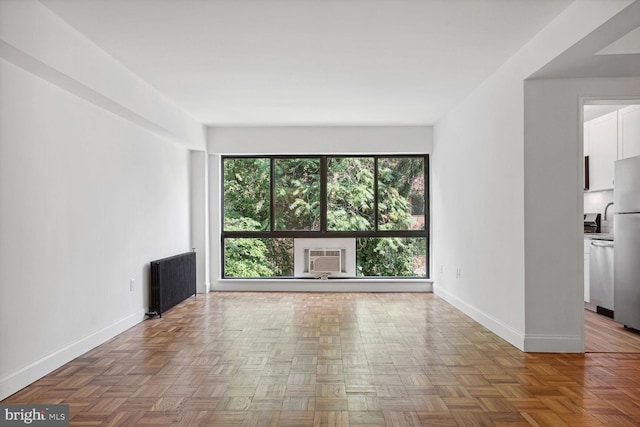 unfurnished living room with a wall mounted air conditioner, parquet floors, and radiator heating unit