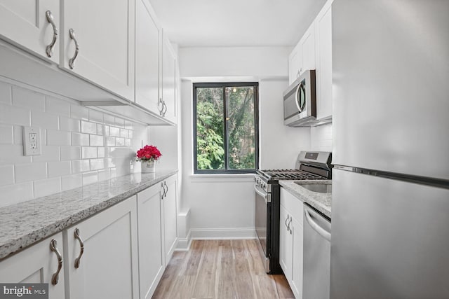 kitchen featuring white cabinets, tasteful backsplash, light hardwood / wood-style flooring, stainless steel appliances, and light stone countertops