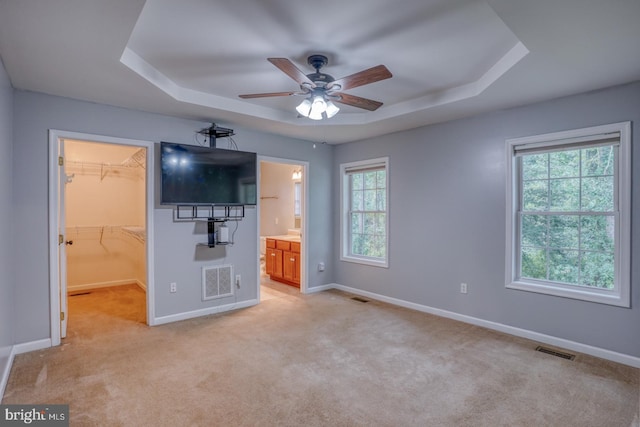 unfurnished bedroom featuring ceiling fan, multiple windows, ensuite bathroom, and a spacious closet