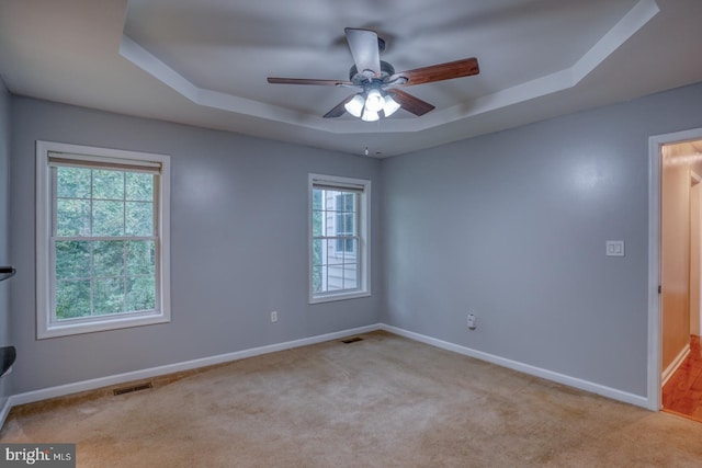 carpeted empty room featuring ceiling fan and a raised ceiling