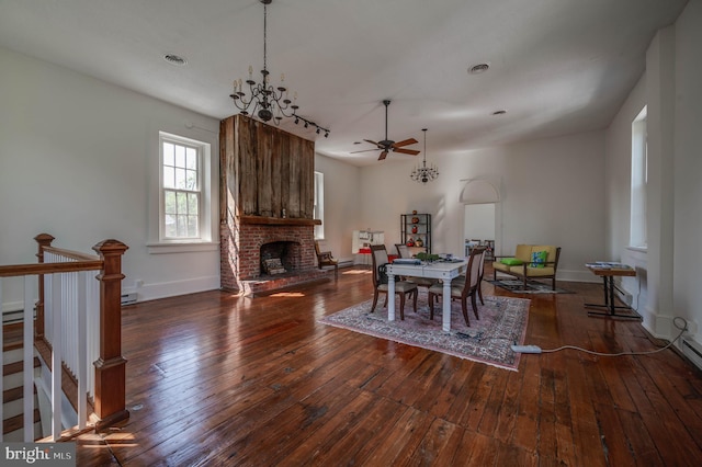 dining space with ceiling fan with notable chandelier, dark hardwood / wood-style flooring, and a brick fireplace