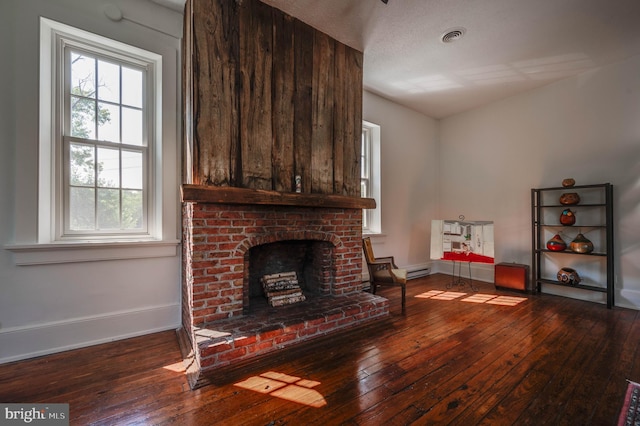 living room featuring baseboard heating, hardwood / wood-style flooring, a fireplace, and a textured ceiling