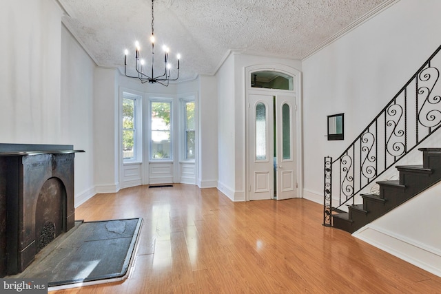 entryway featuring a textured ceiling, ornamental molding, light wood-type flooring, and an inviting chandelier