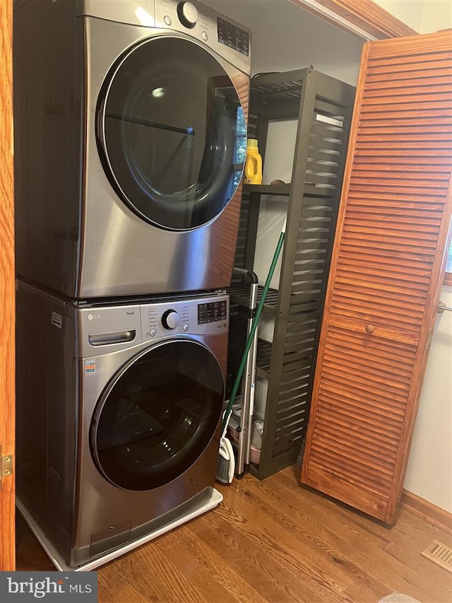 laundry room featuring stacked washer and dryer and wood-type flooring