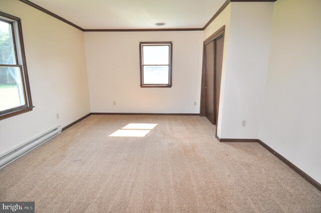 carpeted spare room featuring crown molding, plenty of natural light, and a baseboard heating unit