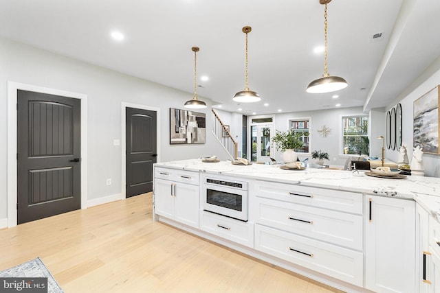 kitchen with light wood-type flooring, light stone counters, oven, white cabinets, and decorative light fixtures