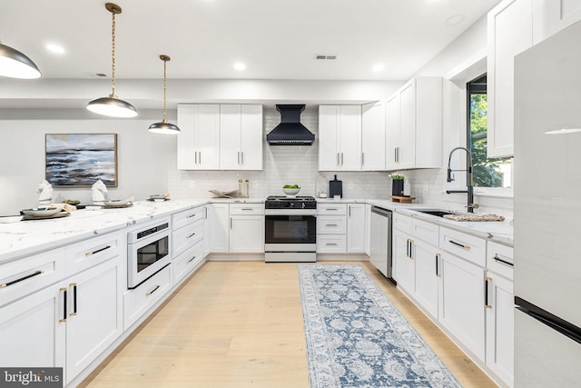 kitchen featuring appliances with stainless steel finishes, hanging light fixtures, white cabinets, and custom range hood