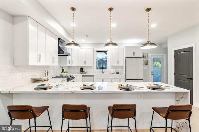 kitchen featuring wall chimney exhaust hood, pendant lighting, white appliances, light stone countertops, and white cabinets